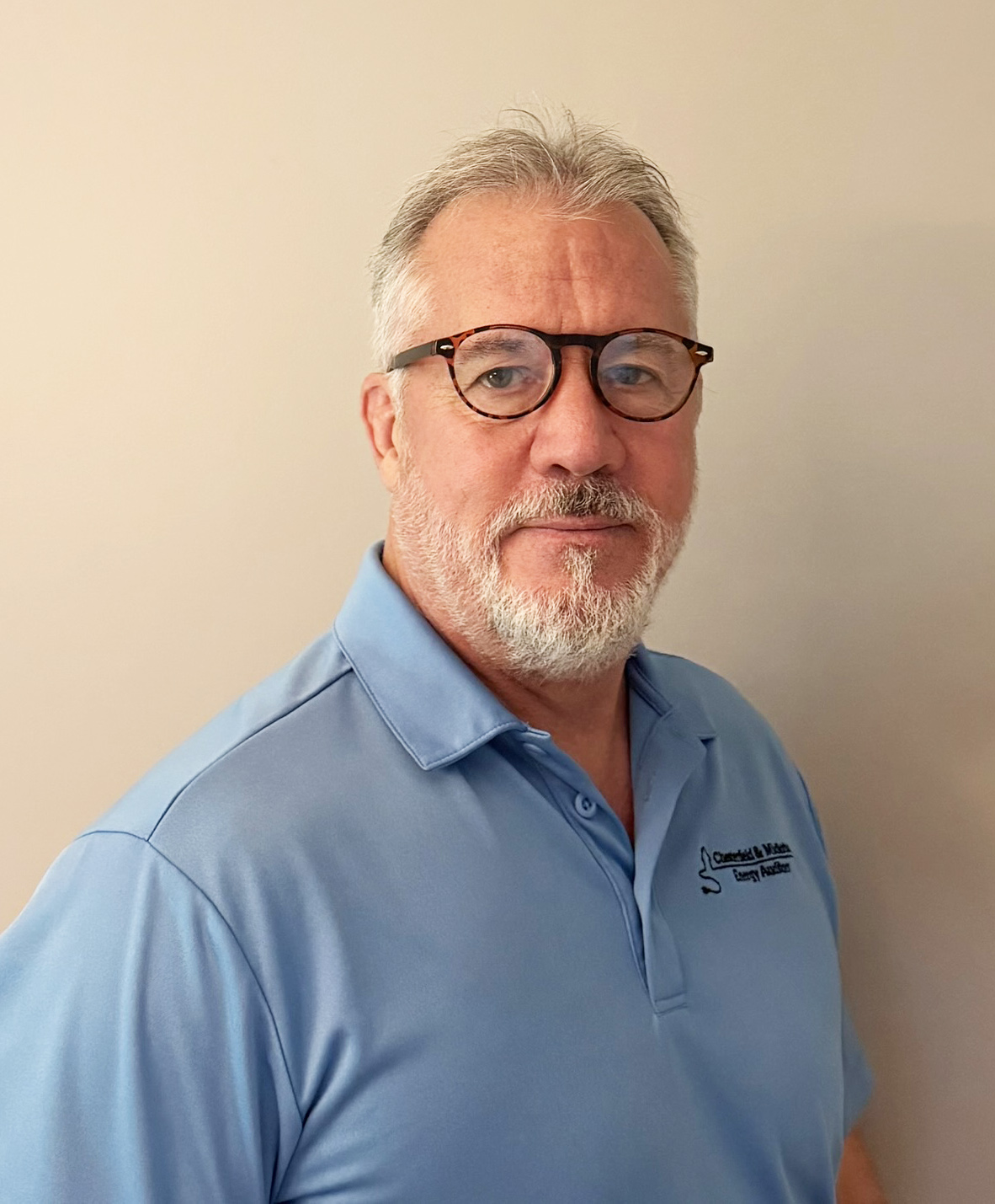 Man with a greying beard and glasses wears a light blue polo shirt
